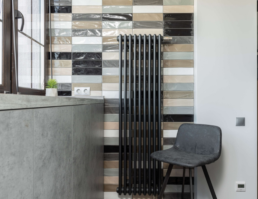 Plan de travail de cuisine avec évier rond en inox, robinet mural chromé, crédence en carreaux blancs et meubles en bois clair, éclairé par une fenêtre avec stores.